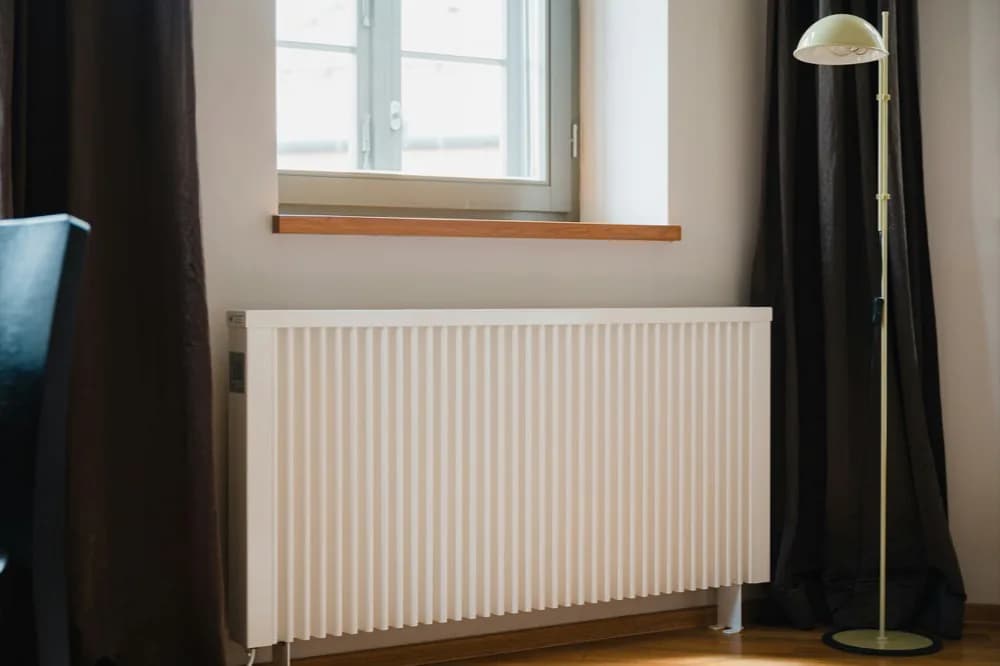 Radiateur blanc à ailettes sous une fenêtre, rideaux tirés