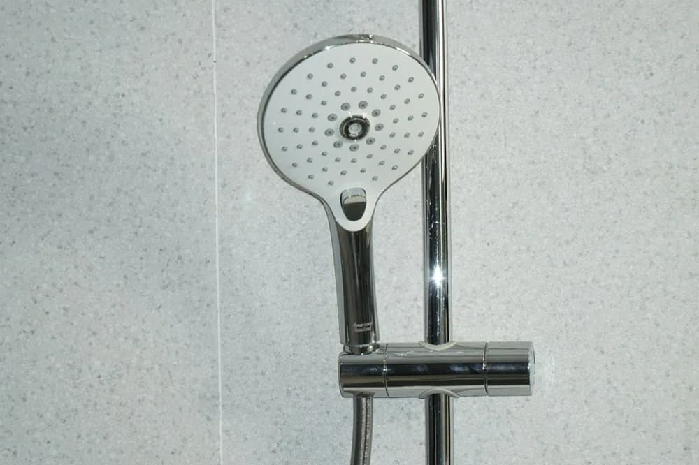 Pomme de douche en acier devant un mur de faïence blanche