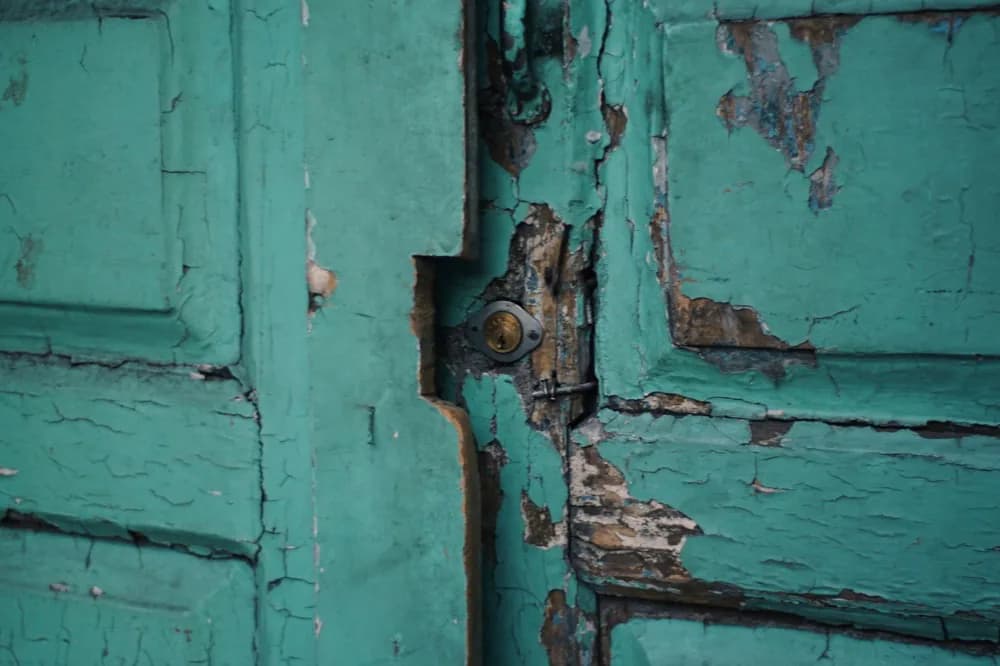Porte de bois dont la peinture bleu vert se soulève en larges écailles