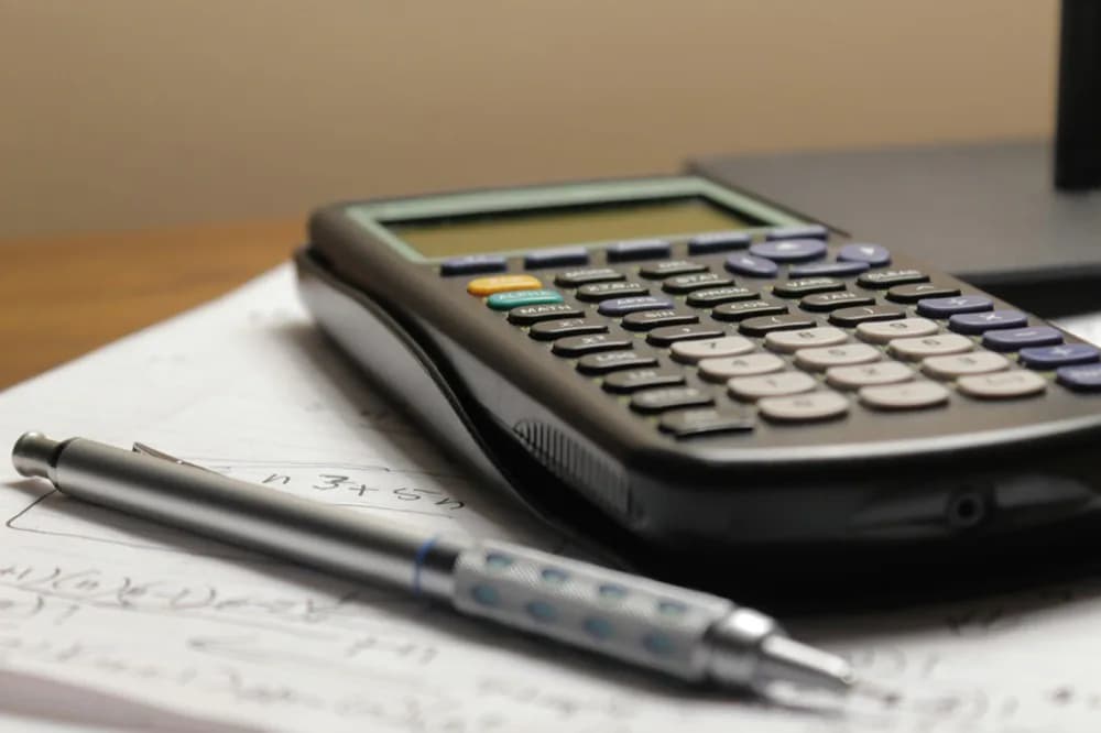 Calculatrice et stylo posés sur une feuille couverte de calculs